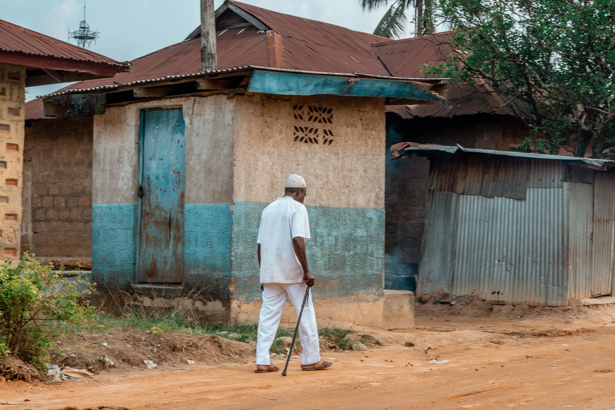 An old man in white pants, shirt and kufi walking in stick in Asaba: A photo by David Elikwu