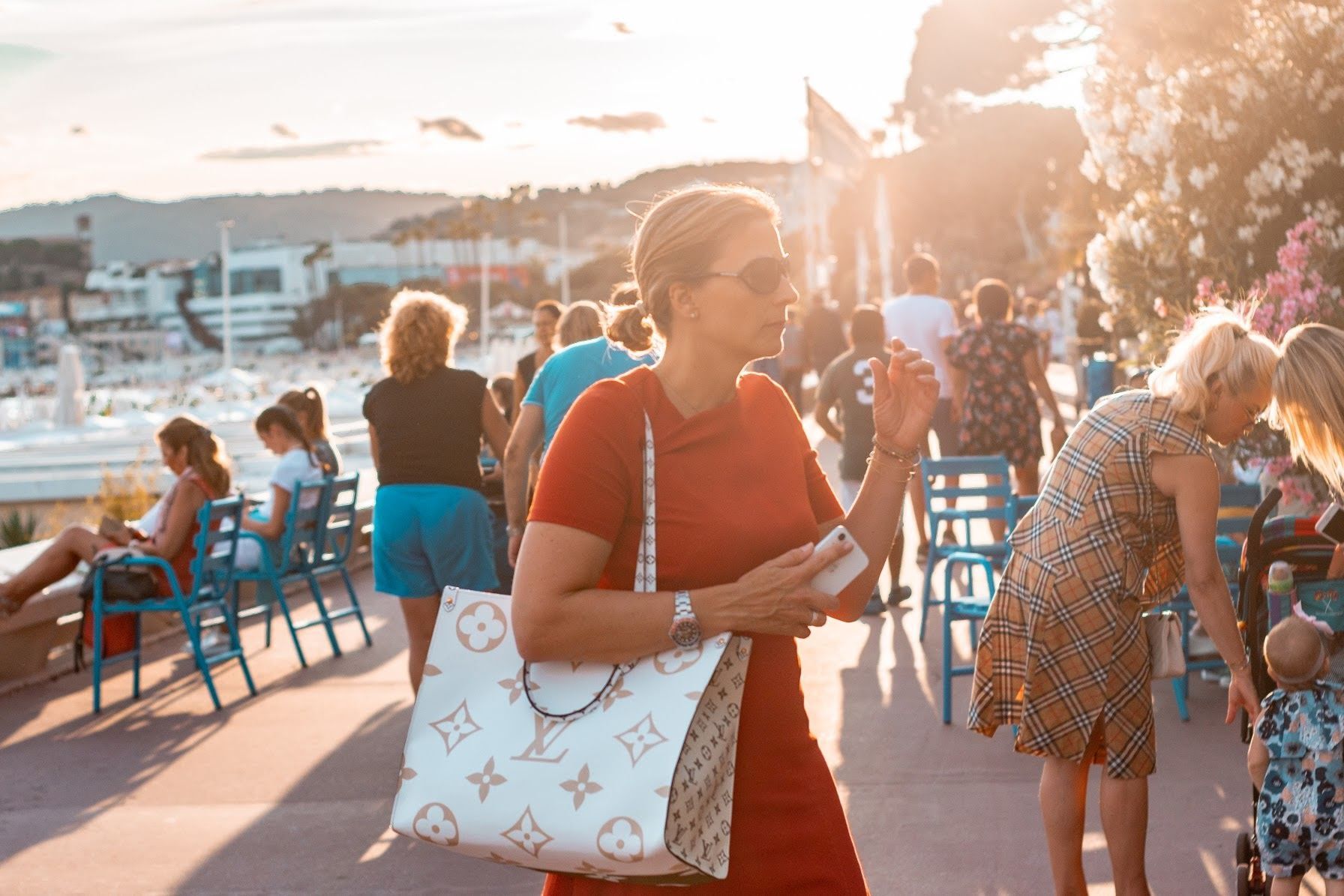 A woman wearing luxury bag and busy people at the background enjoying the sun in Nice: A photo by David Elikwu